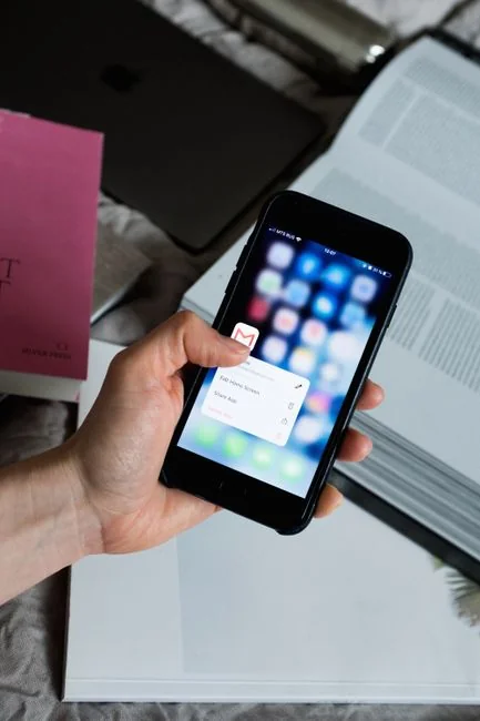 Des mains tenant un smartphone à côté d’un ordinateur portable affichant des graphiques boursiers, illustrant le trading numérique.